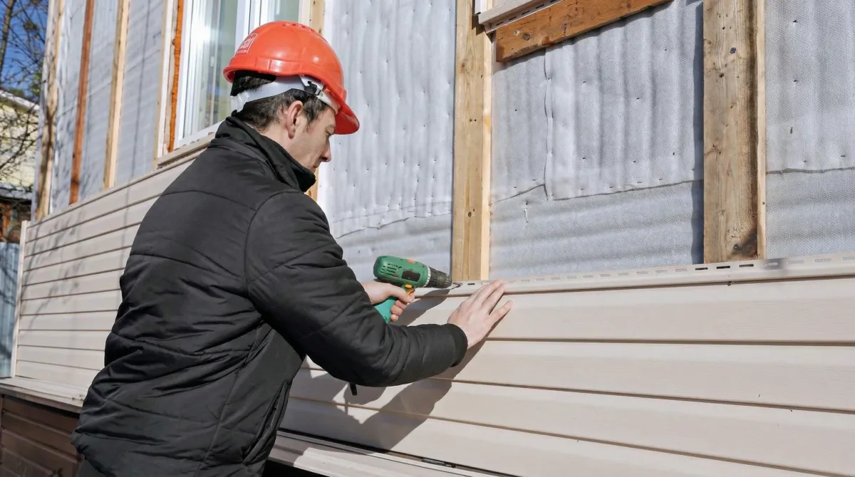 Siding replacement professional using a power drill to install new tan vinyl siding on a home exterior in Green Bay, WI